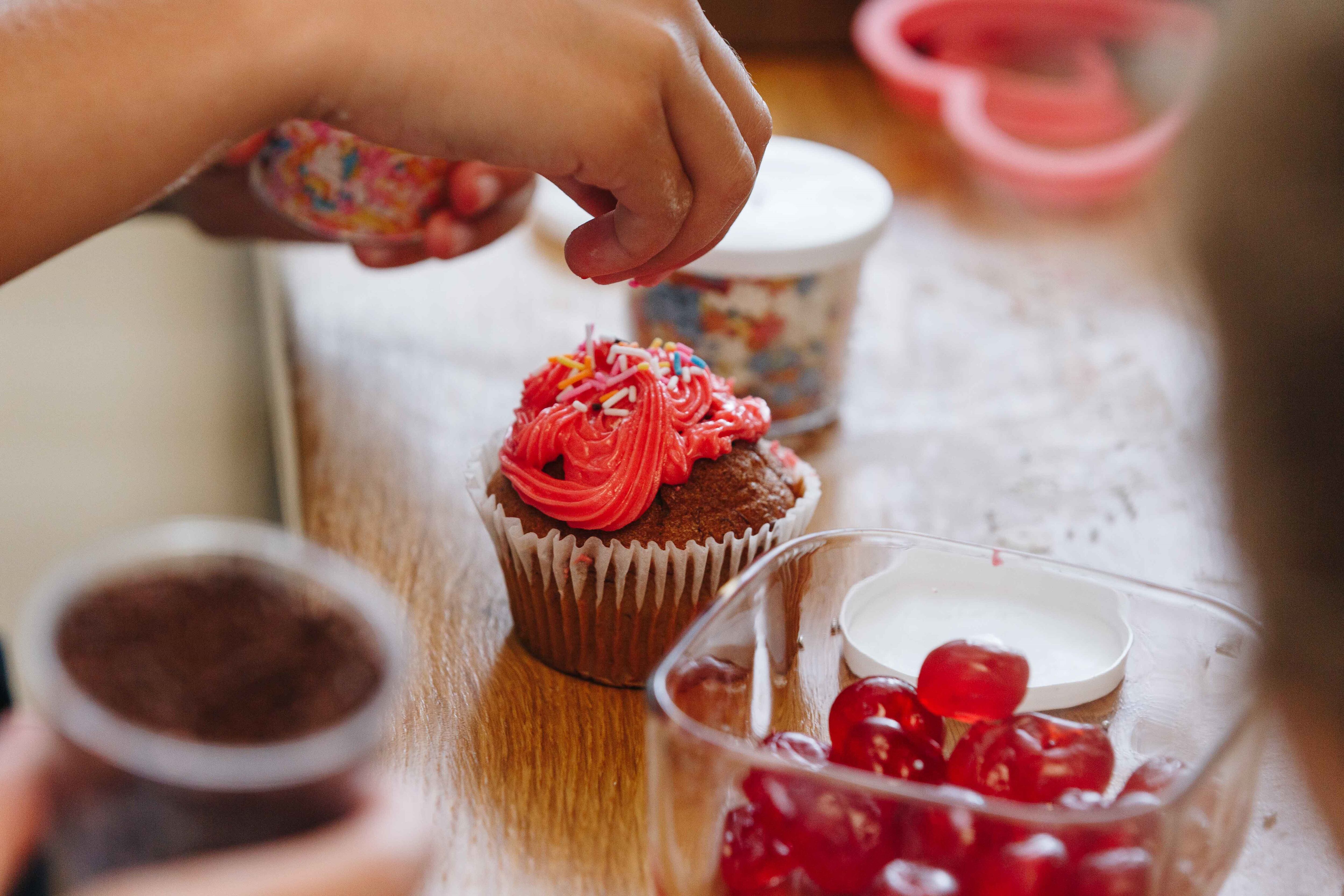 Child decorating a red cupcake