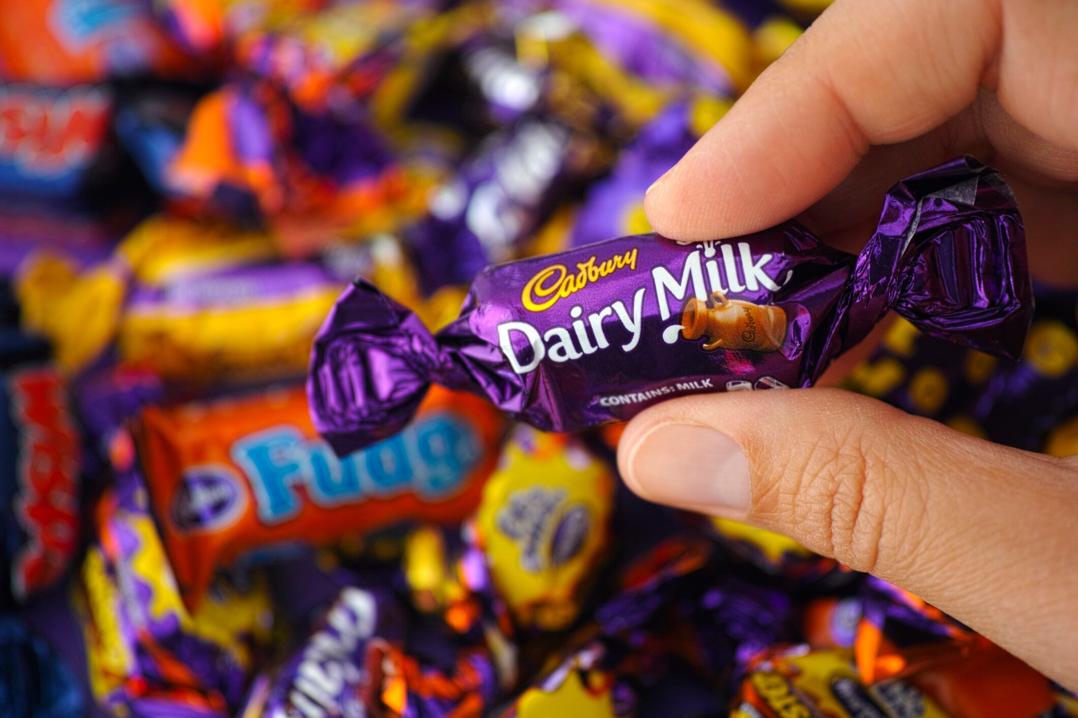 Cadbury Dairy Milk in woman's hand with background of Cadbury chocolates.