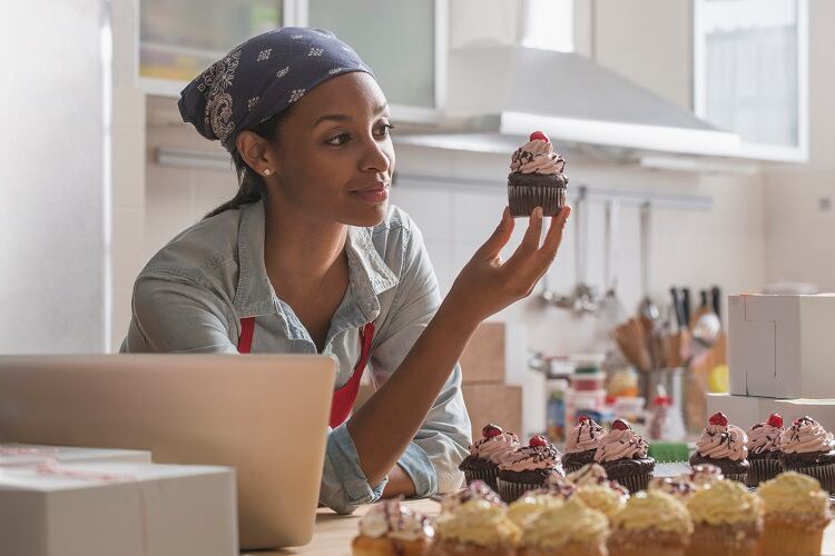 Mixed race baker admiring cupcake in commercial kitchen