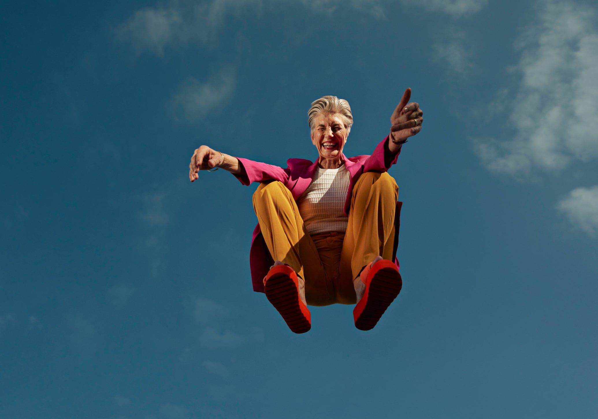 Directly below portrait of happy senior woman crouching mid-air against blue sky