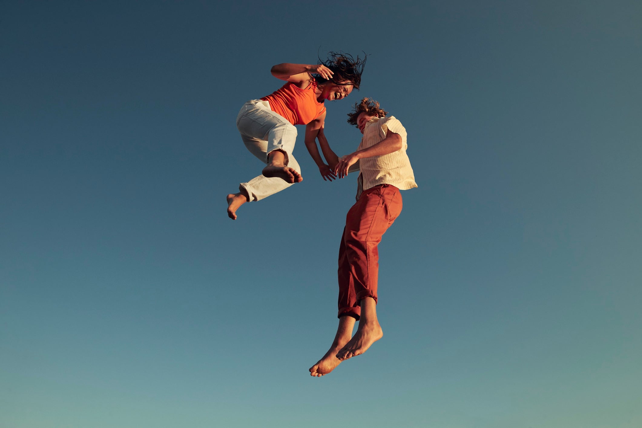 Low angle view of man and woman jumping high up into the air, against clear blue sky.