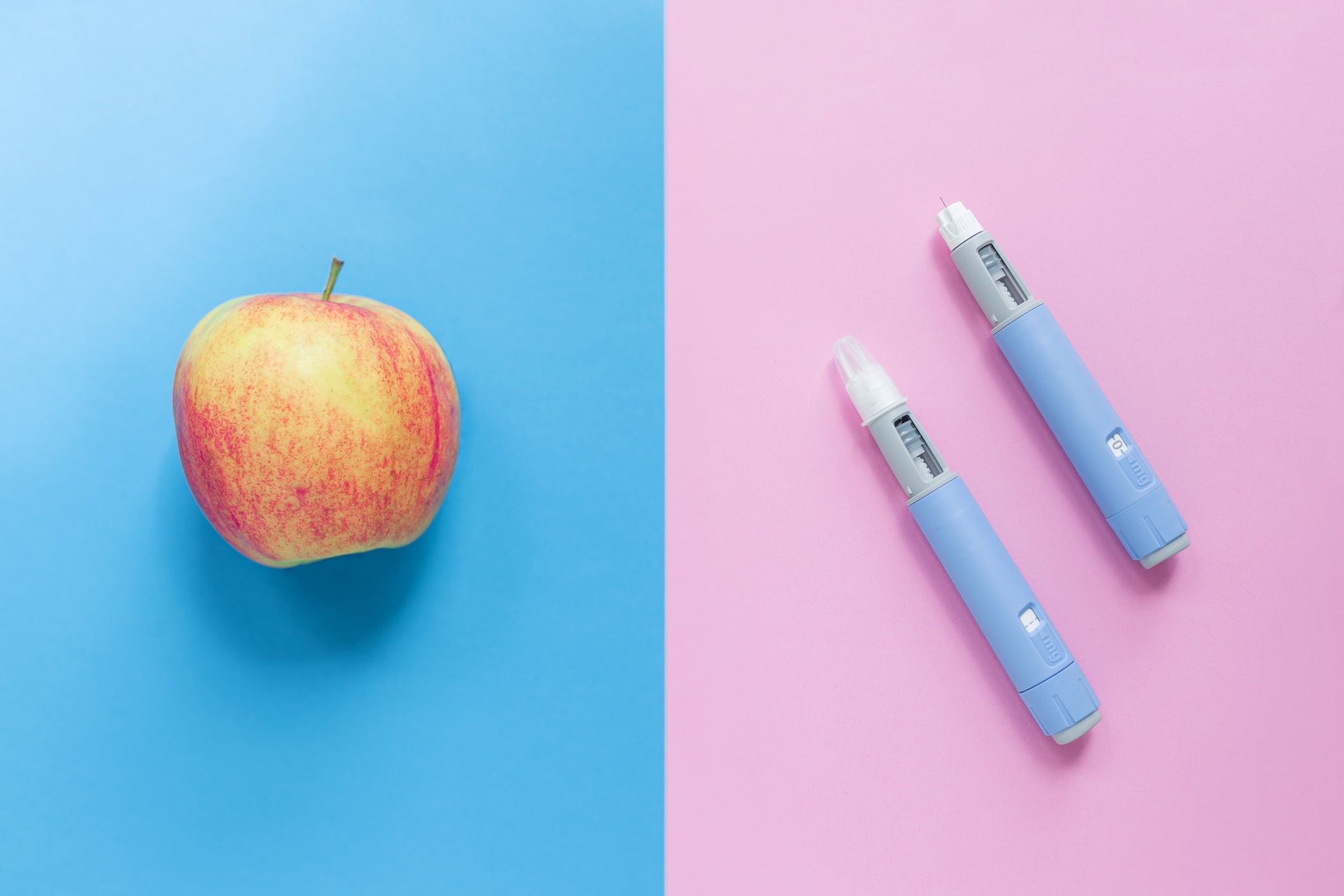 Delicious apple on a blue background and two injectors dosing pens for subcutaneous injection of antidiabetic medication or anti-obesity medication on a pink background. Weight loss, concept