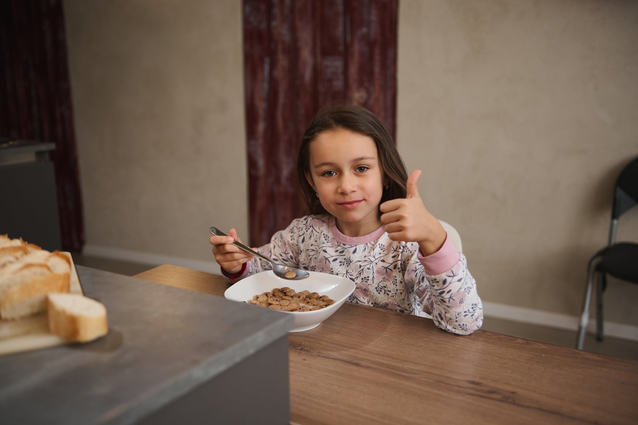 Smiling girl giving thumbs up while eating breakfast cereal at home