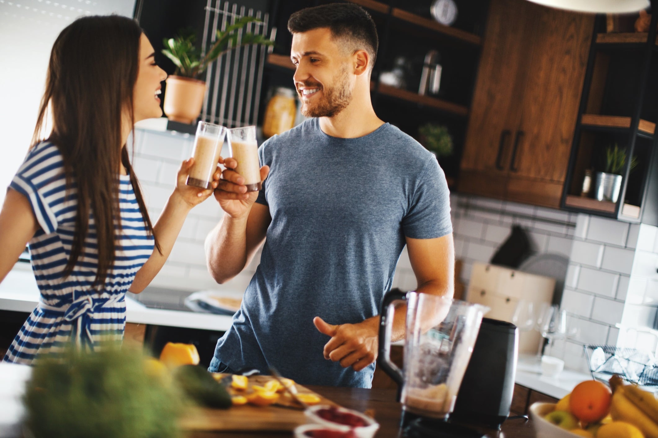 Young couple making healthy drink in their kitchen. They are smiling and toasting with juices.