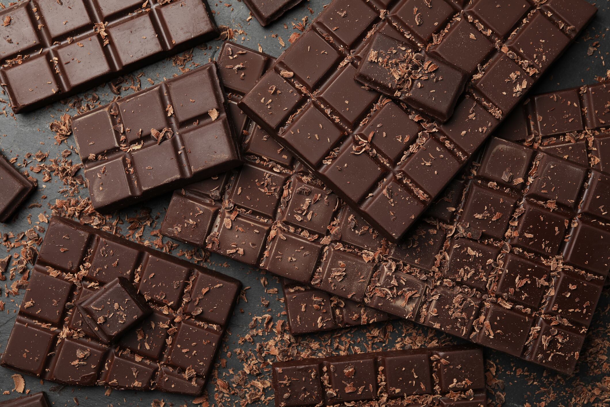 Pieces and shavings of tasty chocolate bars on grey table, flat lay