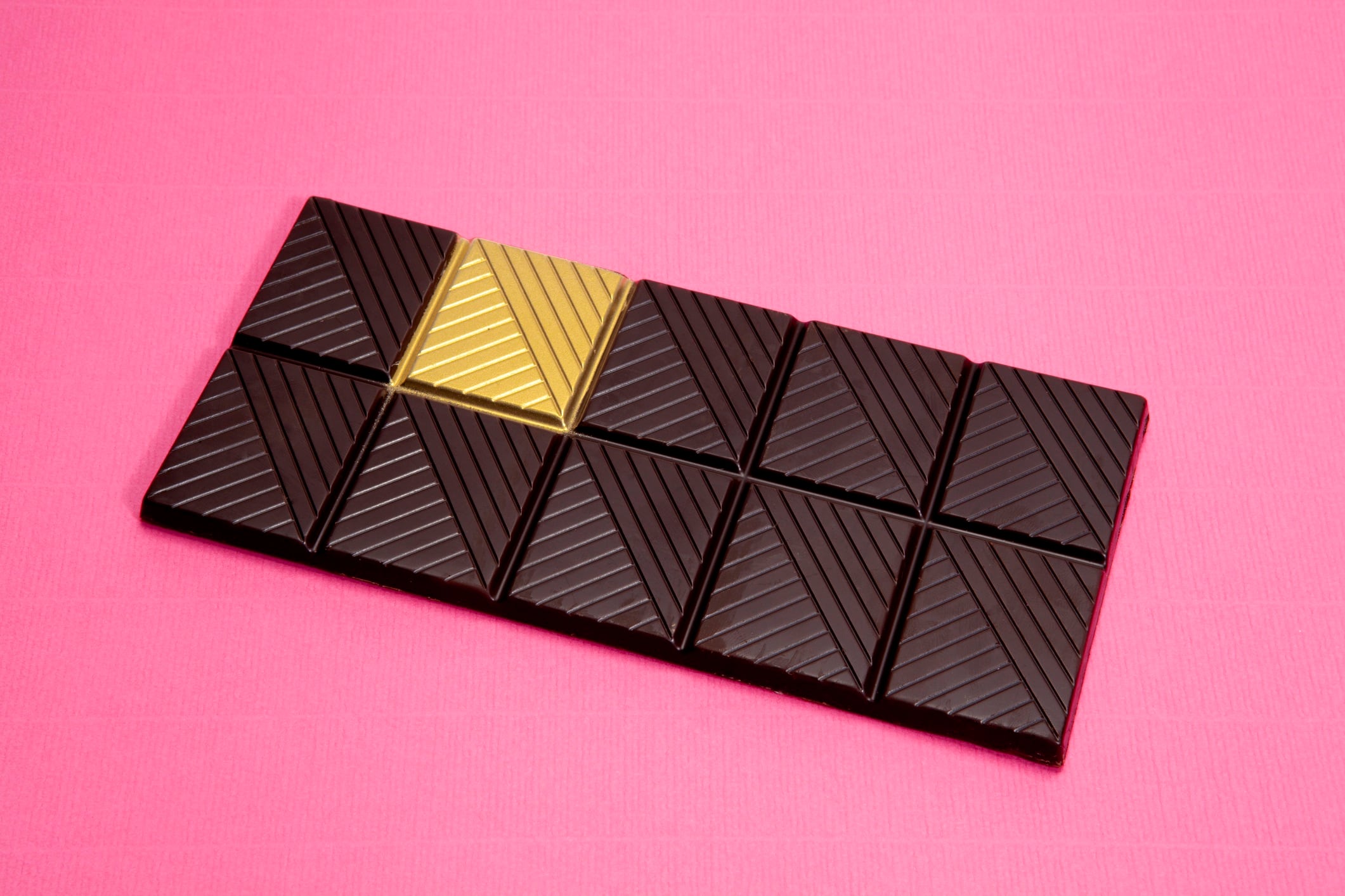 A whole dark chocolate bar with a gold square isolated on a pink background.