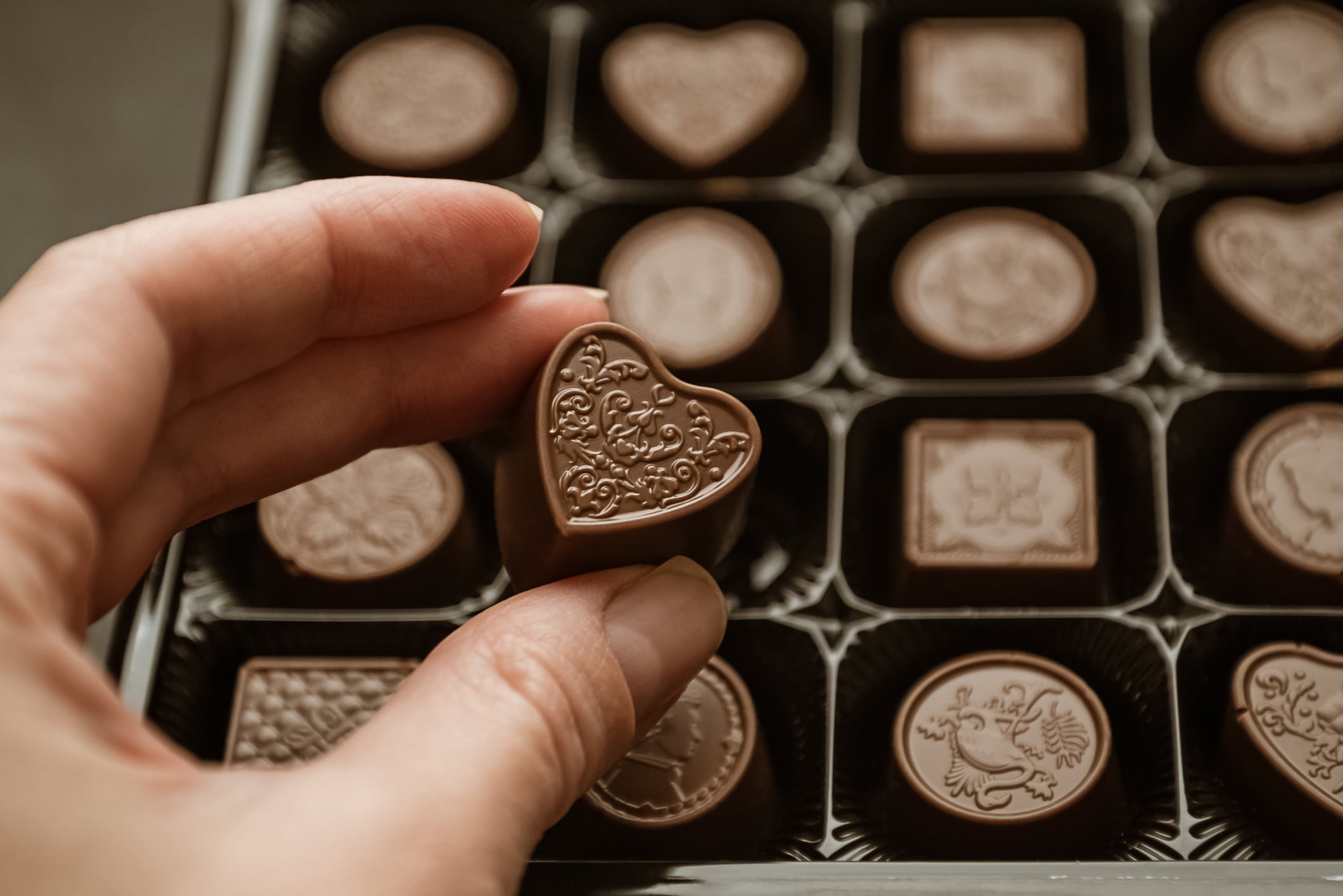 Person taking heart-shaped chocolate sweet from candy box
